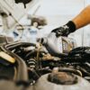 Een fles versnellingsbakolie, 2-takt olie en een olieopvangbak op een werkbank, klaar voor gebruik bij motoronderhoud.