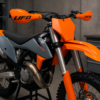Motocross motor met nieuwe oranje/grijze UFO plastic kit en UFO handkappen, gemonteerd met bijpassende bevestiging set in een professionele werkplaats.