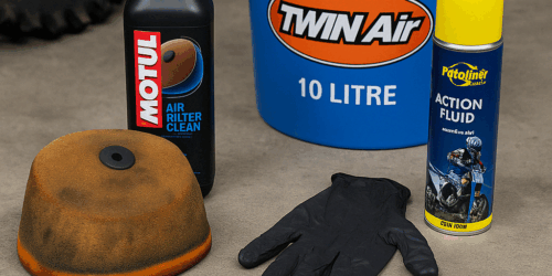 Een vies luchtfilter naast een emmer met cleaner, luchtfilterolie en onderhoudshandschoenen, klaar voor schoonmaak in een crossgarage