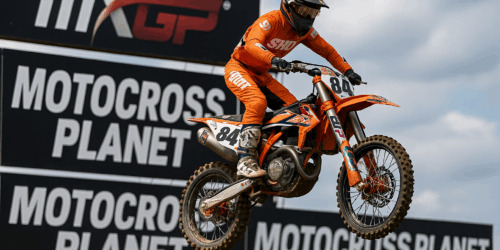 Een motorcrosser op een KTM racemotor vliegt door de lucht tijdens een MXGP-wedstrijd, met banners van Motocross Planet op de achtergrond