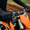 Close-up van een crosser met zwarte motorcross handschoenen die stevig het stuur vasthoudt op een modderige baan