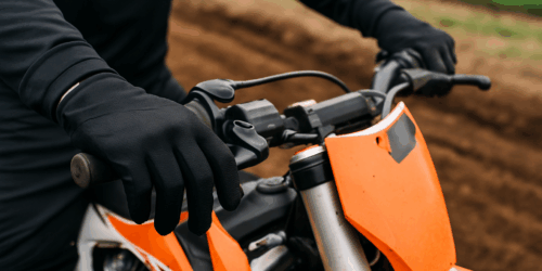 Close-up van een crosser met zwarte motorcross handschoenen die stevig het stuur vasthoudt op een modderige baan