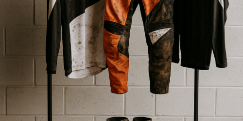 Motorcross kleding hangt te drogen aan een rek na een modderige rit, met helm, laarzen en handschoenen netjes uitgespreid in een garage