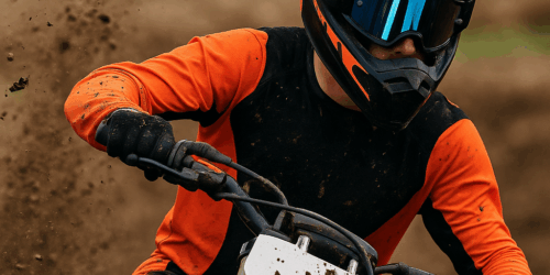 Een motorcrosser met spiegelende crossbril in actie op een modderige baan, modderspatten vliegen omhoog richting het gezicht