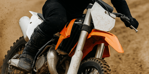 Een motorcrosser in actie op een zanderige baan, met duidelijke focus op zijn zwarte kniebeschermers tijdens het nemen van een bocht