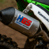 Close-up van een HGS uitlaat met carbon eindkap gemonteerd op een Kawasaki crossmotor tijdens een modderige motorcross training