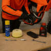 Een crosser sleutelt in een garage aan zijn KTM motor terwijl onderdelen, olie en gereedschap verspreid liggen op de werkbank