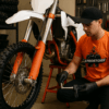 Een motorcrosser monteert nieuwe onderdelen aan zijn crossmotor in een goed uitgeruste werkplaats