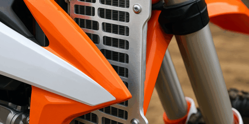 Een zilveren radiator guard op een witte en oranje crossmotor, gemonteerd met bouten en zichtbaar tussen de kappen