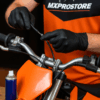 Een crossmonteur monteert een nieuwe gaskabel op een crossmotor, met vet en tang zichtbaar op een houten werkbank
