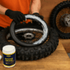 Een monteur legt een mousse in een crossmotorband met montagevet op een houten werkbank, terwijl het wiel klaarstaat voor montage