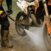Crosser spuit modder van zijn motor met reiniger – focus op ketting, wielen en frame