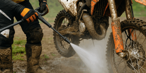 Crosser spuit modder van zijn motor met reiniger – focus op ketting, wielen en frame